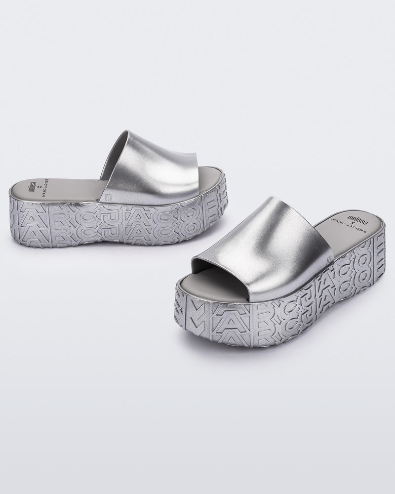 An angled front and side view of a silver Melissa Becky platform slides with the Marc Jacob's logo across the sole.