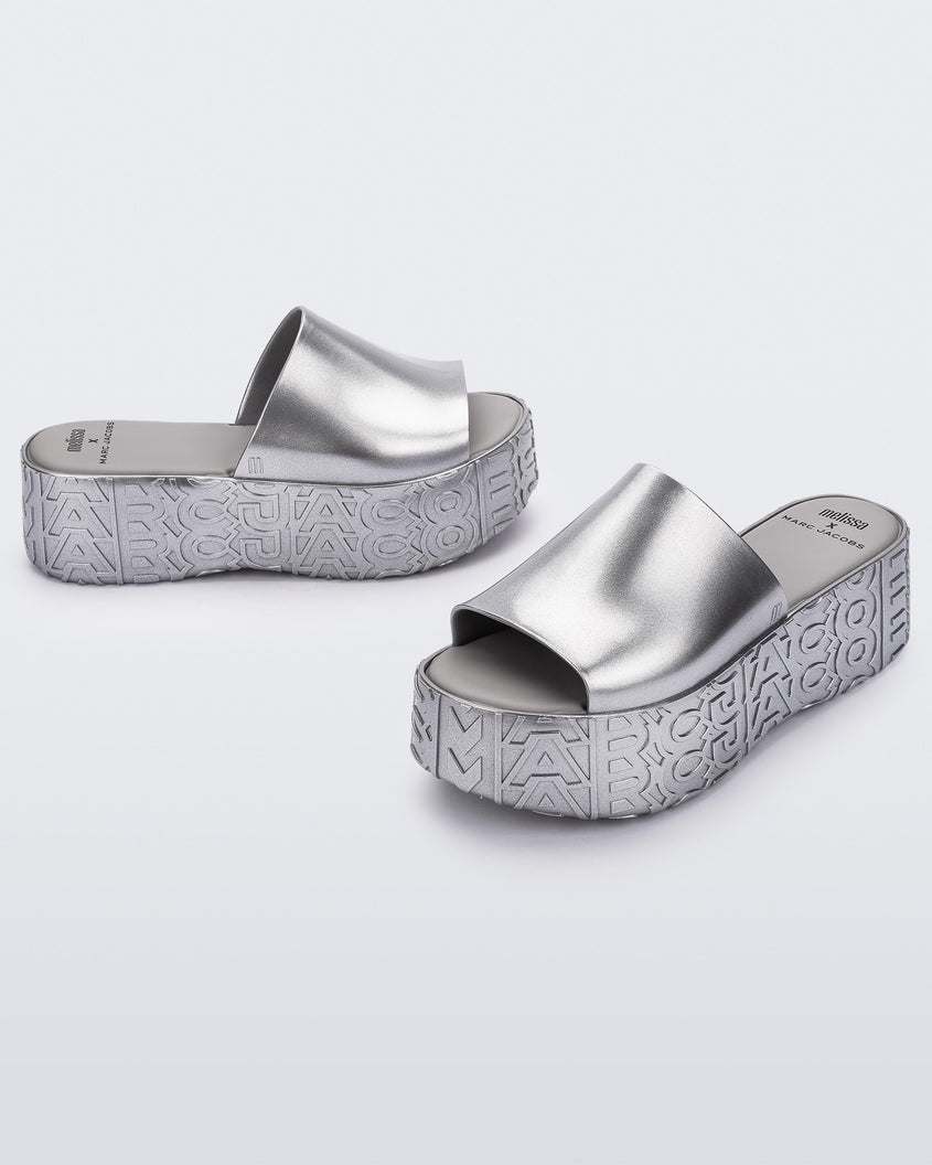 An angled front and side view of a silver Melissa Becky platform slides with the Marc Jacob's logo across the sole.