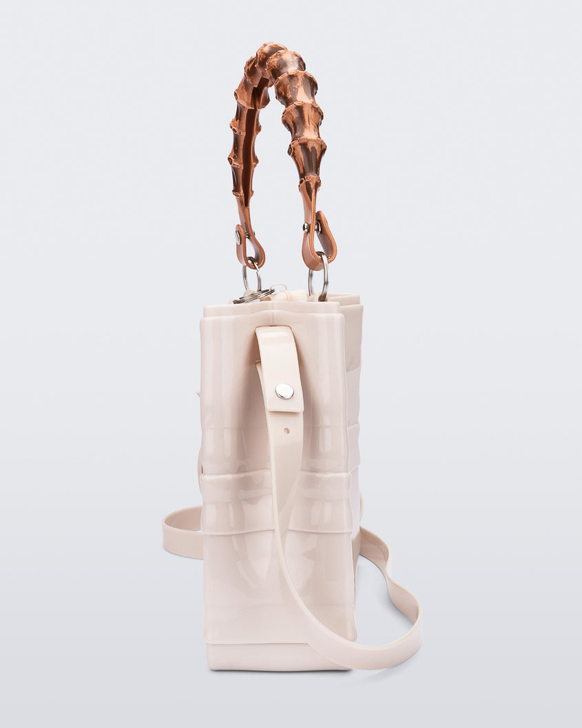 A side view of a beige Melissa Tie Bag with a bow detail on the front, two bamboo top straps and a beige shoulder strap.