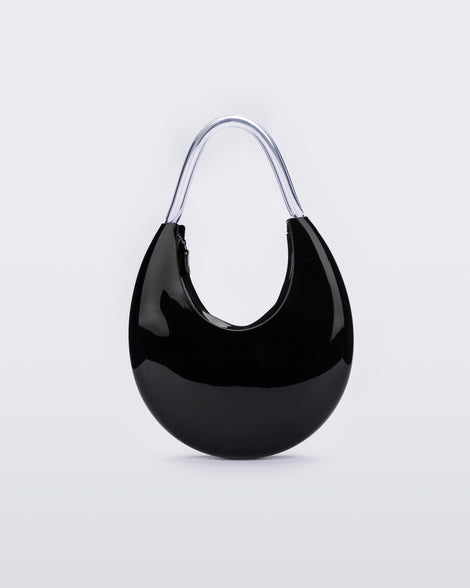 Back view of the Melissa Moon Handbag. The body of the bag is crescent shaped and is black with a top zipper closer. There is a short shoulder handle that is clear / transparent material. the back side is smooth and does not contain any exterior details/ pockets