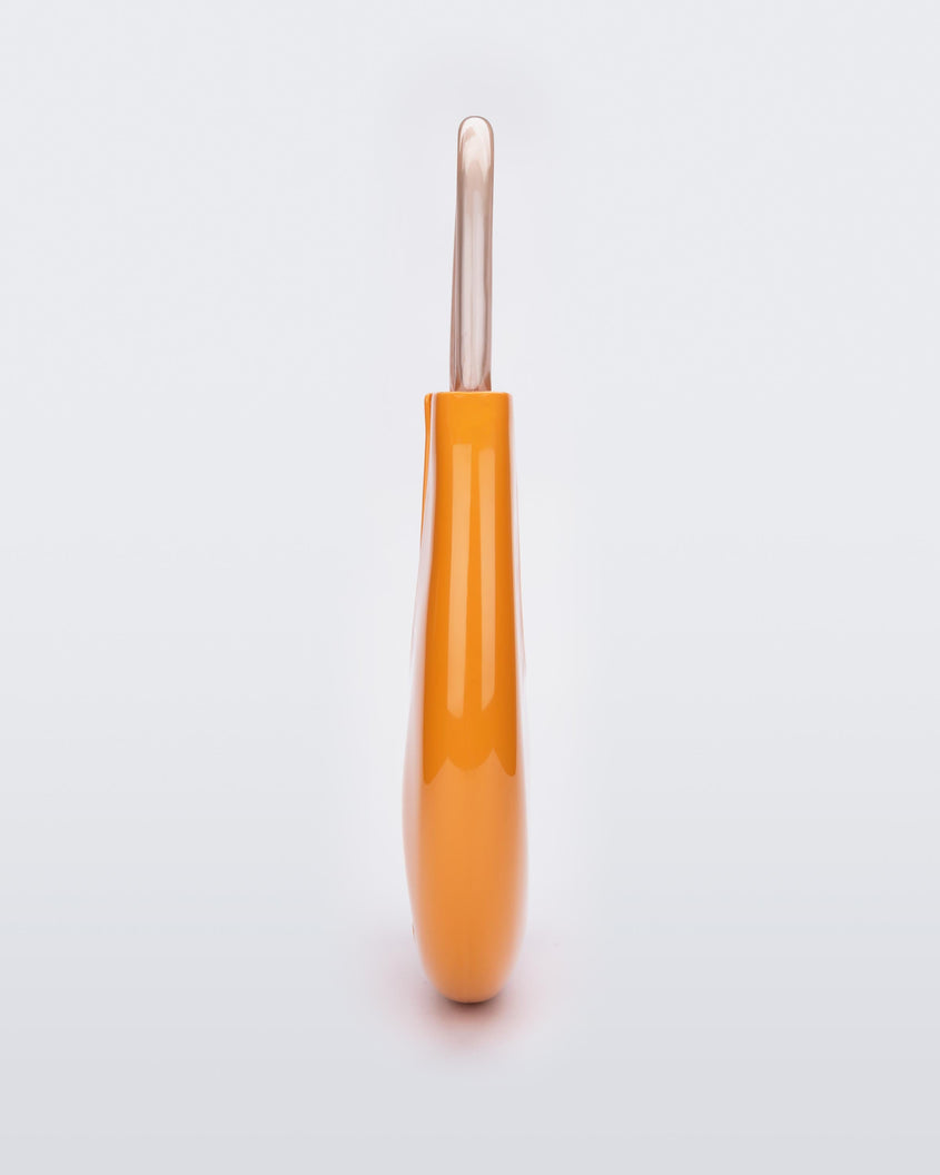 A side view of a orange/beige Melissa Moon Bag with a crescent shaped orange bag base and a clear beige top strap.
