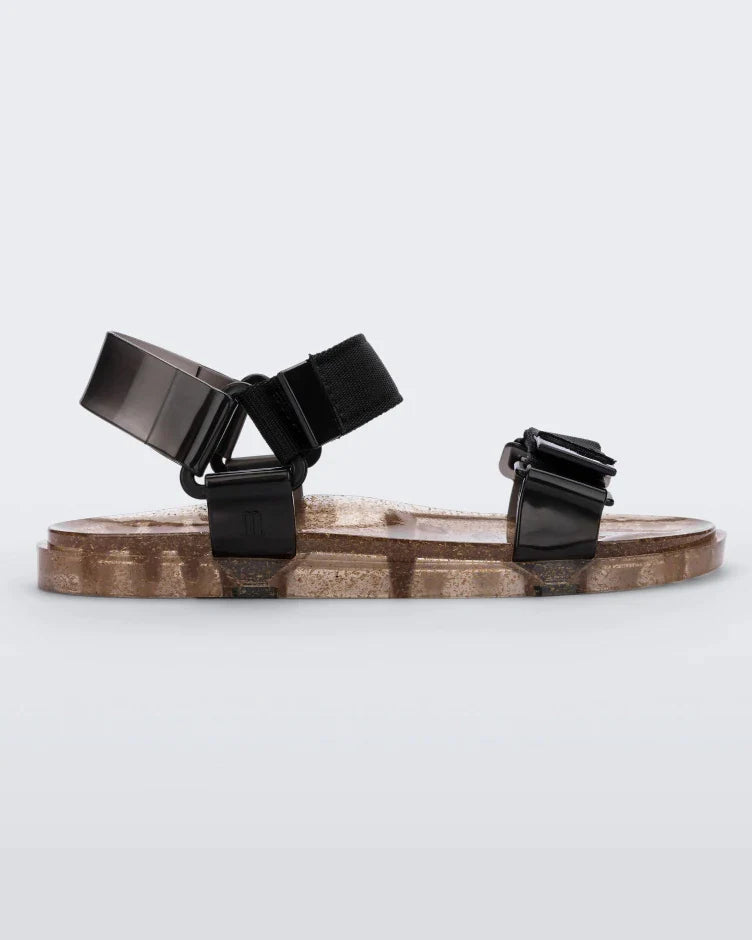 Side view of a Melissa Wide Papete sandal with transparent gold glitter sole with black velcro straps
