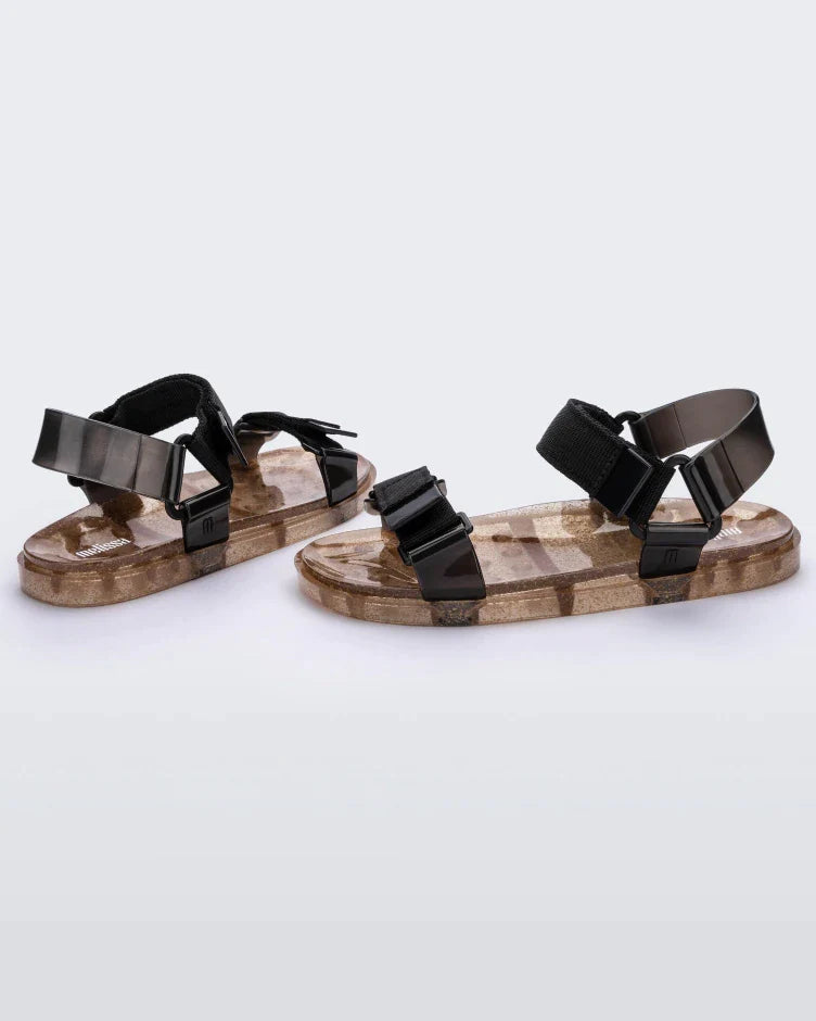 Angled view of a pair of Melissa Wide Papete sandals with transparent gold glitter sole with black velcro straps