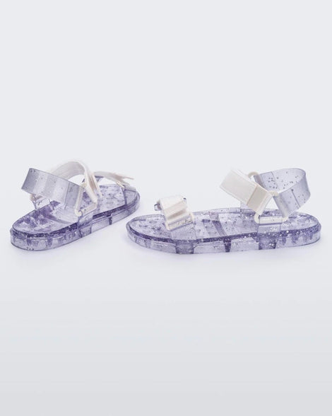Angled view of a pair of Melissa Wide Papete sandals with transparent silver glitter sole with white/clear velcro straps