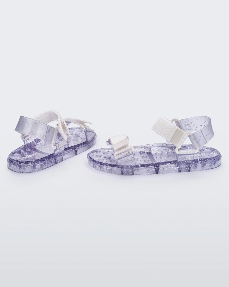 Angled view of a pair of Melissa Wide Papete sandals with transparent silver glitter sole with white/clear velcro straps