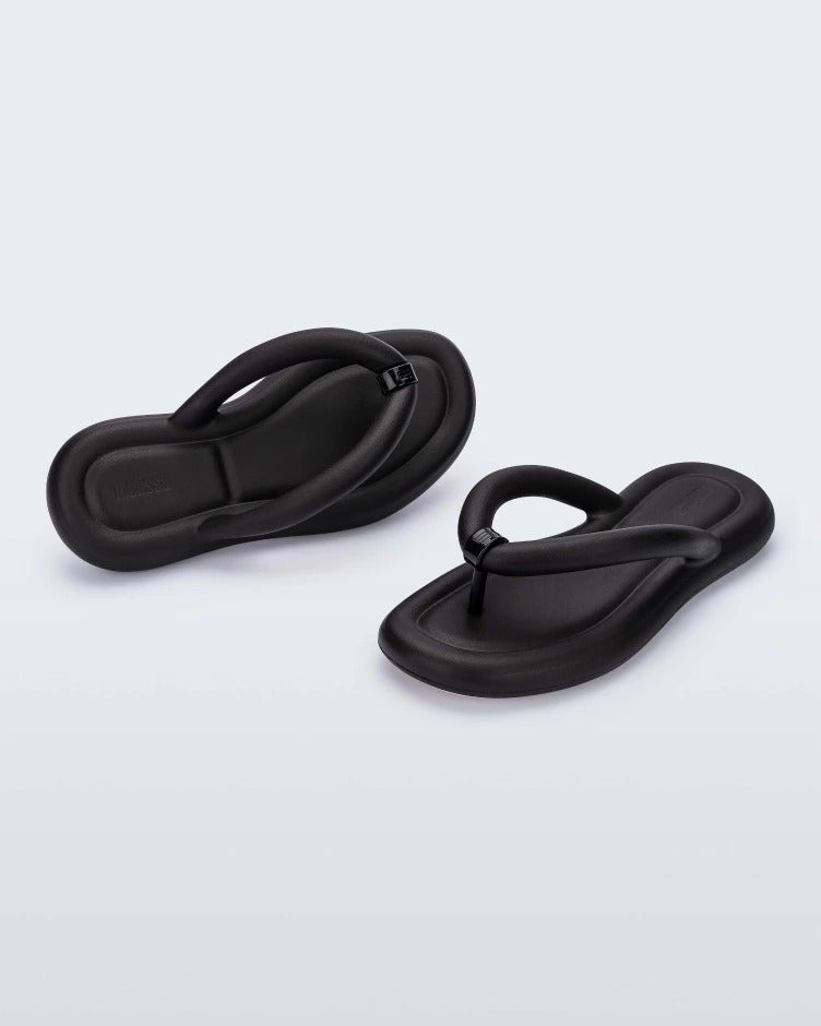 An angled back and front view of a pair of black Melissa Free Flip Flops with puffer-like straps.