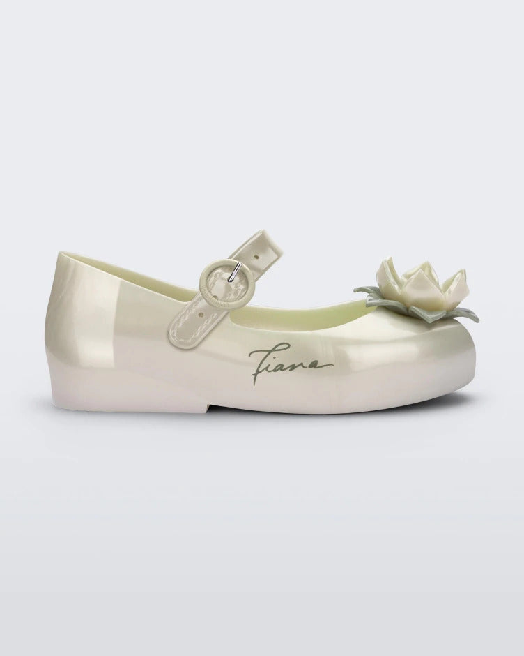 Side view of a Metallic White/Green Mini Melissa Sweet Love Princess flat with a metallic white base with Tiana in script on the side, a top strap, a flower detail on the toe and a drawing of Tiana of The Princess and The Frog on the insole.