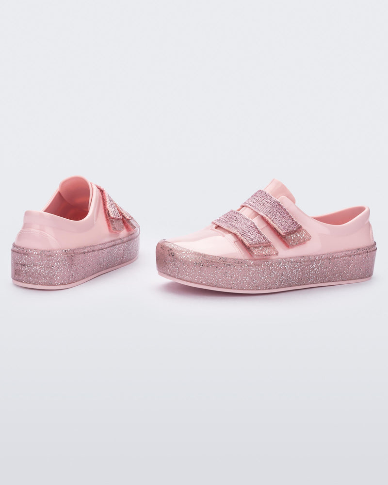 An angled side and back view of a pair of Pink/Pink Glitter Mini Melissa Beanny Bugs sneakers with a pink base, two shiny pink velcro straps and a pink glitter sole.