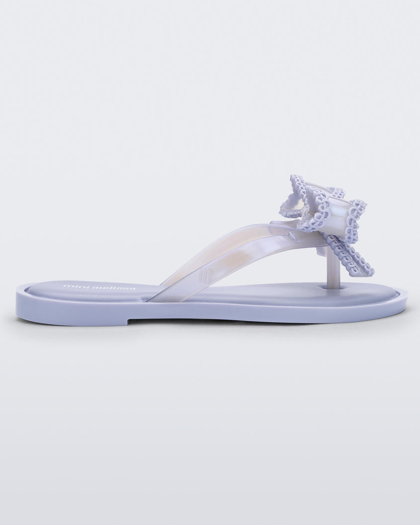 Side view of a lilac Mini Melissa Slim flip flop with a lace like bow detail on the front strap.
