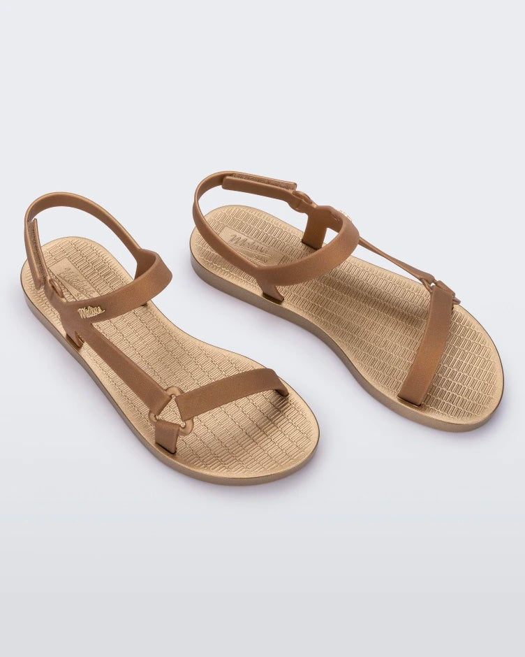 Top view of a pair of gold metallic Melissa Sun Downtown sandals with a front and ankle strap joined together by a vertical strap and a triangle buckle.