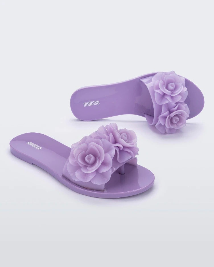 An angled top and side view of a pair of lilac Melissa Babe Garden slides with two flowers on the front strap.