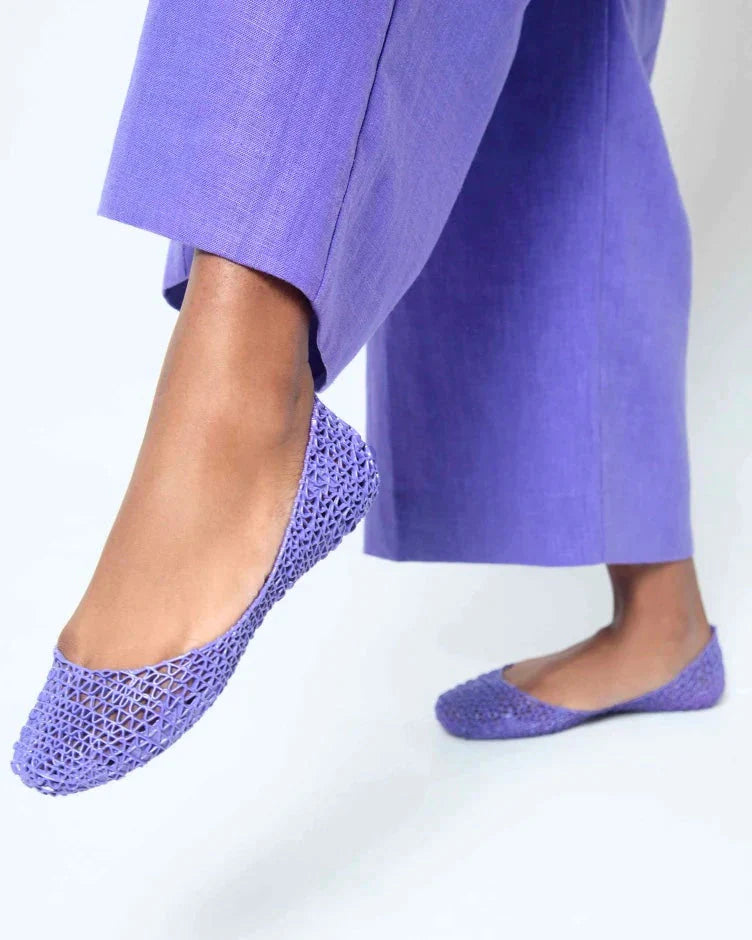 A close up of a person wearing a pair of Melissa Campana purple flats with matching purple pants.