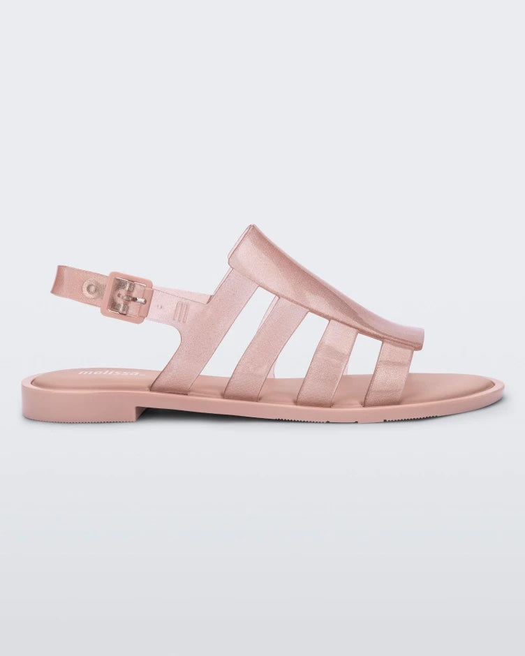 Side view of a transparent glitter pink Melissa Boemia sandal with straps conjoining in the front and a back buckle.