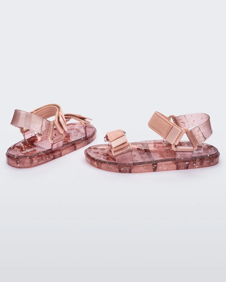 Angled view of a pair of Melissa Wide Papete sandal with transparent pink glitter sole with pink velcro straps