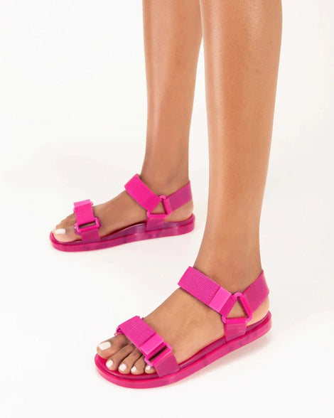 A model's legs waring a pair of Melissa Wide Papete sandals in pink with velcro ankle and front straps.