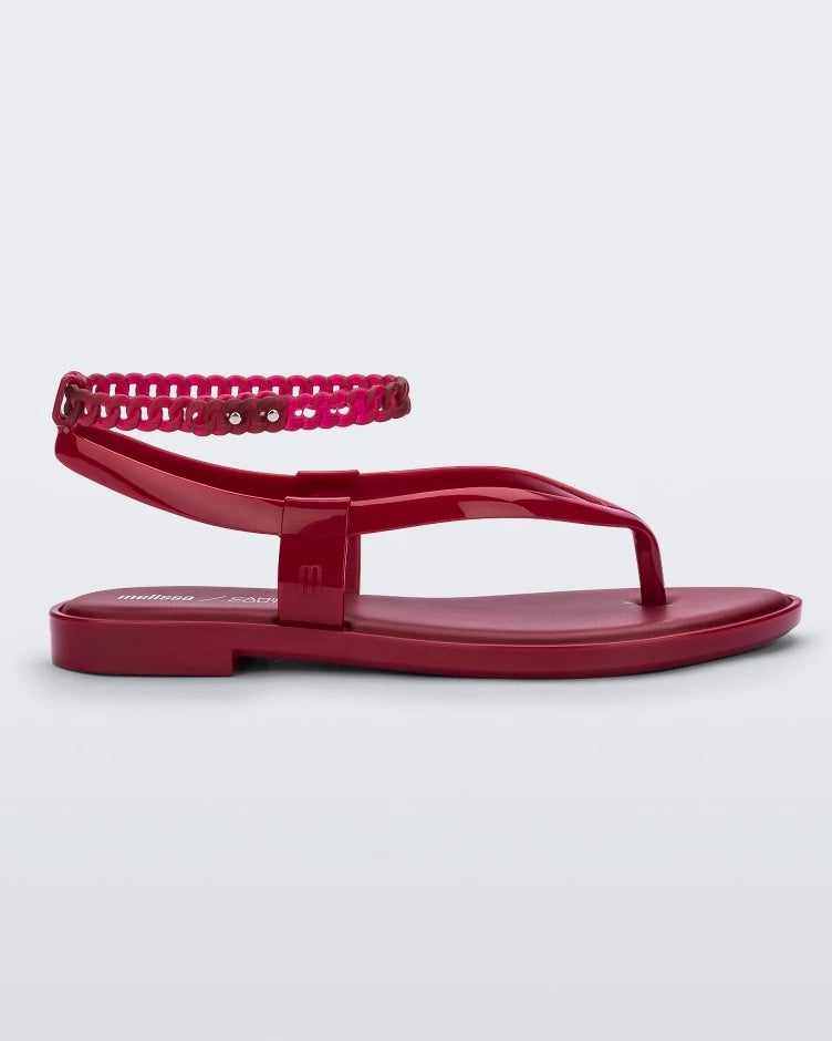 Side view of a red Melissa Unique sandal with flip flop straps and a woven detail ankle strap.