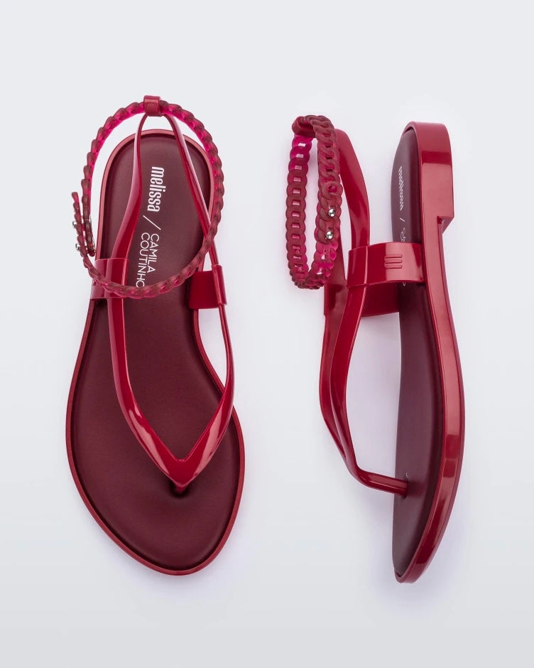 A top and side view of a pair of red Melissa Unique sandals with flip flop straps and a woven detail ankle strap.