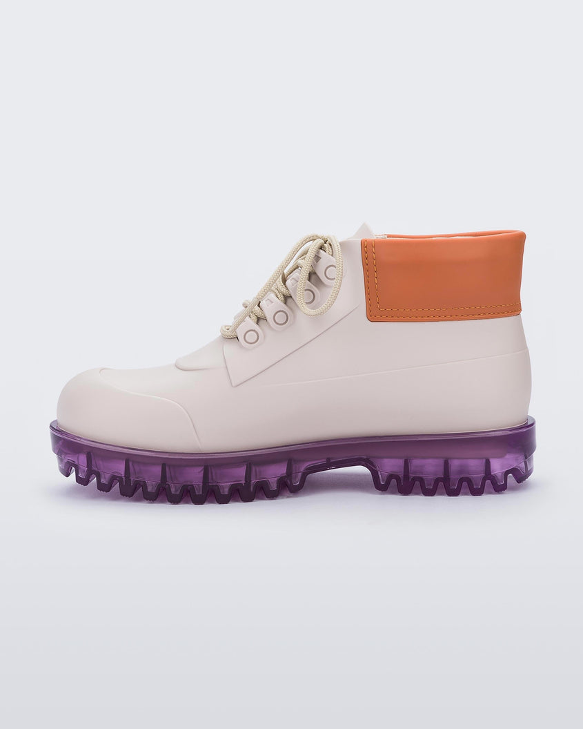 An inner side view of a beige/orange/lilac Melissa Ares combat boots with a beige base, beige laces, orange top back and translucent lilac sole, on a blue and orange background.