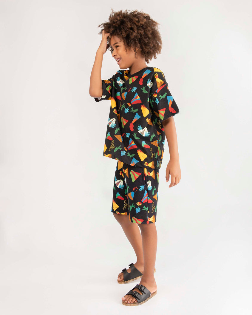 A young model posing for a picture in black patterned top, bottom and a pair of Black/Beige Mini Melissa Wide Slides with a black top with two black buckles and a beige sole.