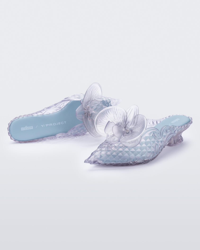 Top and angled view of pair of Melissa Flower Court mules in clear with kitten heel and a 3D flower above the toe. The top view shows the light blue colored insole
