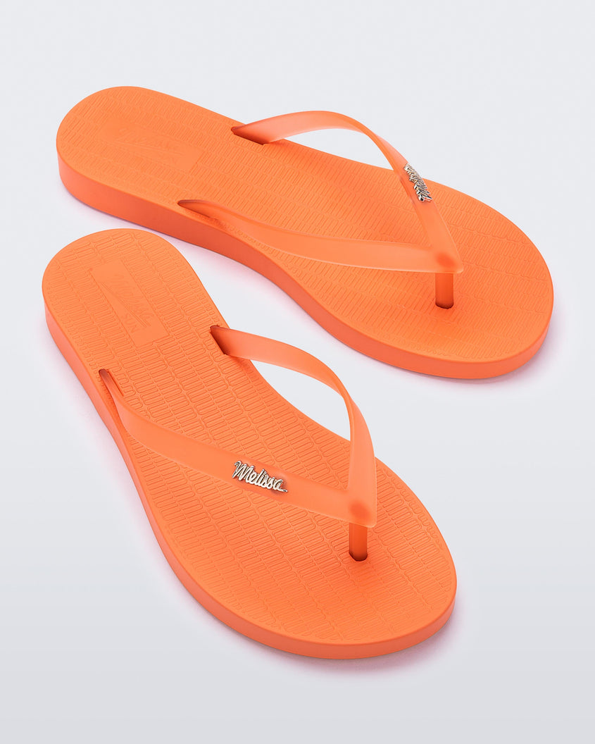 An angled top view of a pair of orange Melissa Sun Venice flip flops with