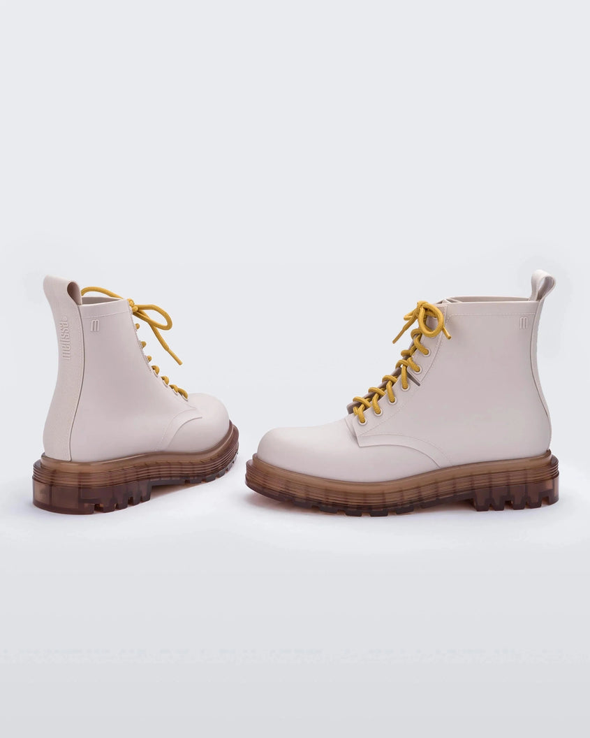 An angled back and side view of a pair of matte beige/yellow Melissa Coturno boots, with a matte beige base, yellow laces and a brown sole.