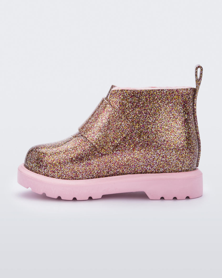 An inner side view of a pink/glitter multicolor Mini Melissa Chelsea boot with a multicolor glitter base, velcro front strap and a pink sole.