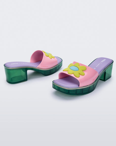 Angled view of a pair of Melissa Shape slides with green platform heel, a pink wide front strap with a yellow and blue flower on the top of the strap and a purple insole