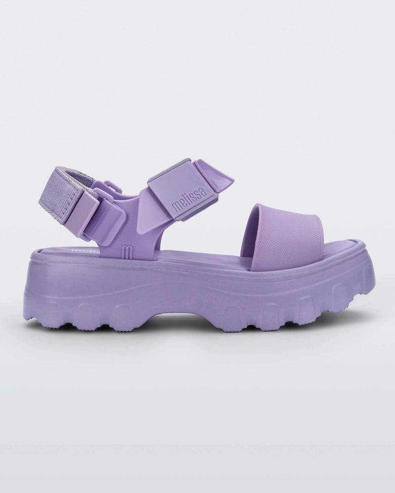 Side view of the Melissa Kick Off platform sandal in lilac. The sandal has an ankle strap with a plastic clasp closure on the front ankle side, additional velcro adjustable strap is on the back of the ankle strap.