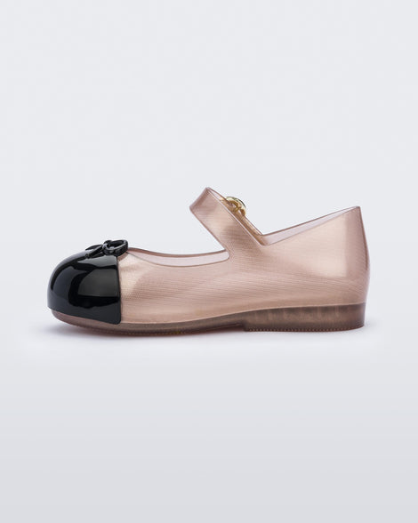 Inner side view of the Mini Melissa Sweet Love ballet flat with buckle strap. The body of the shoe is a transparent rose gold color, the shoe has a black cap to with a 3D bow applique on the top of the toe. The buckle hardware on the strap is gold.