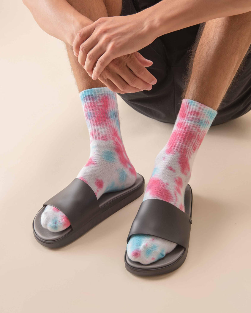A model posing wearing a pair of black Melissa Beach slides with tie dye socks.