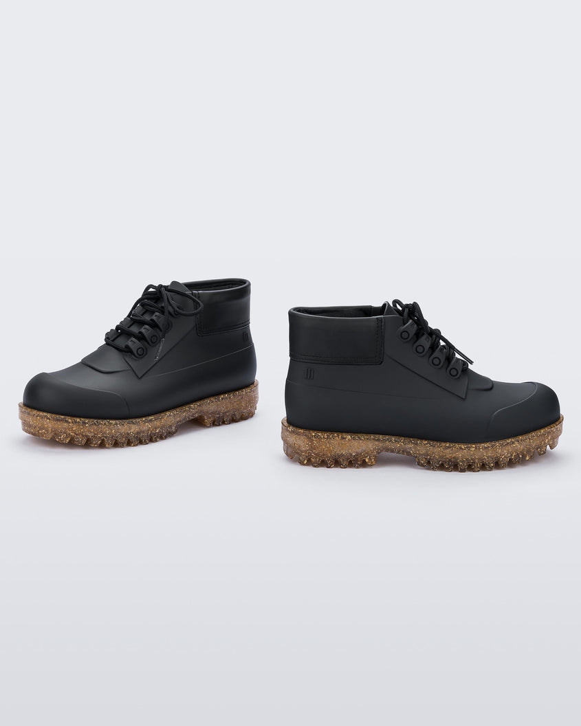 An inner and outer side view of a pair of matte black / rice husk Melissa Ares combat boots with a black sole, black laces and brown / gold glitter rice husk tractor sole.