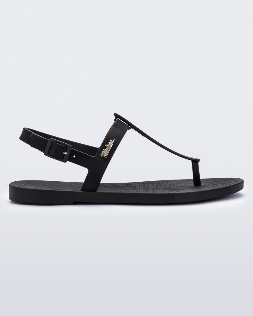 An outter side view of a black Melissa Sun Ventura sandal with a top strap, reading melissa in silver, intersected by a vertical front strap detail and an ankle strap.