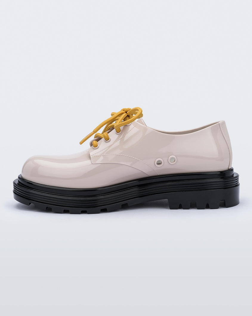 An inner side view of a beige Melissa Bass sneaker with a beige base, yellow laces and a black sole.