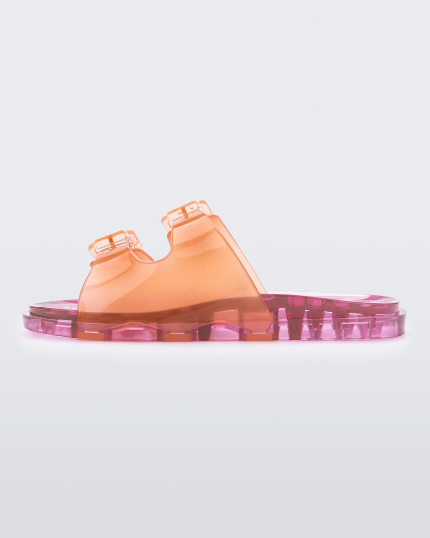An outter side view of an orange/pink Mini Melissa Wide Slide with an an orange top with two silver buckles and a pink sole.