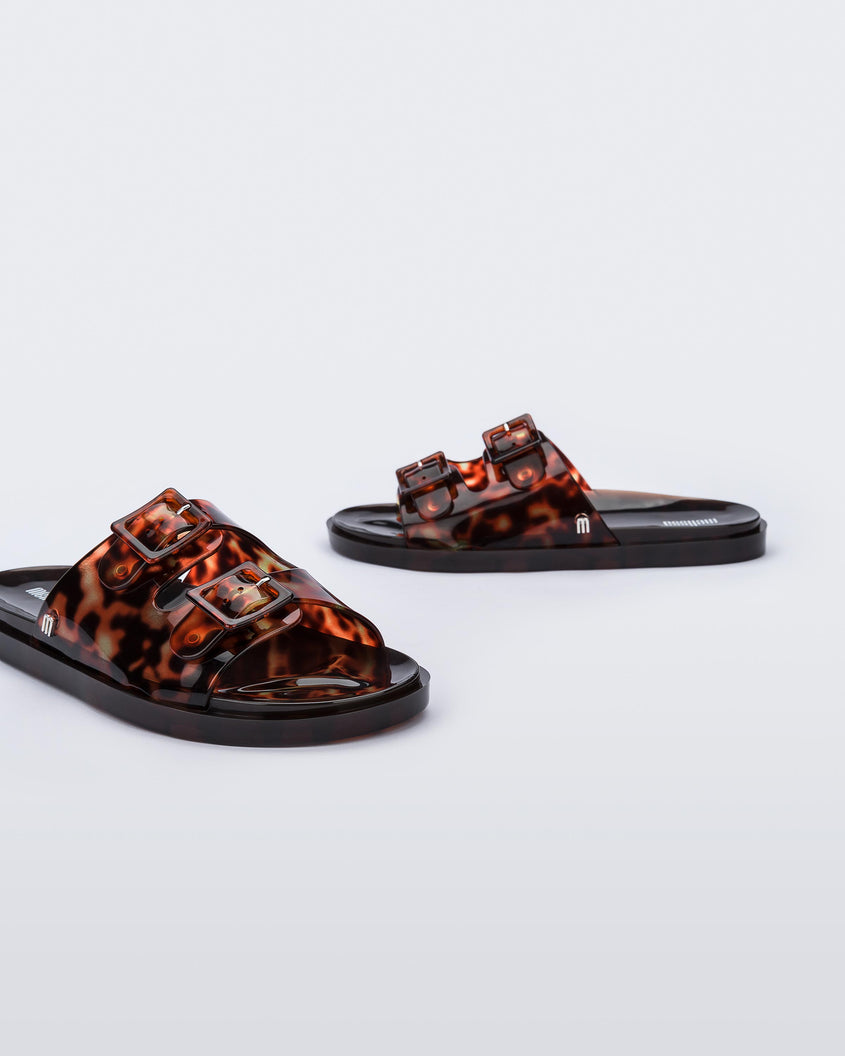 Angled view of a pair of Melissa Wide slide sandals with brown sole and brown tortoise colored straps