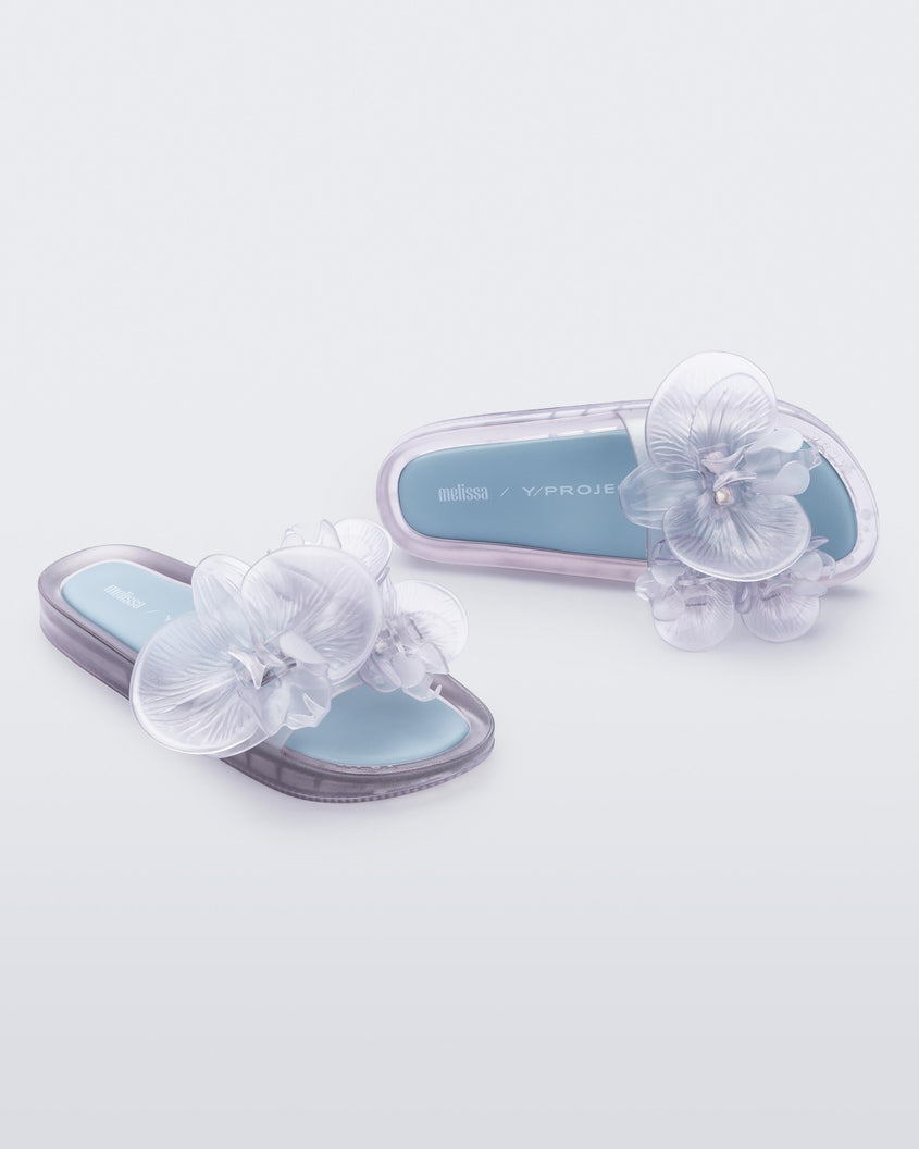 Top and angled view of a pair of Melissa Flower Beach slide in Clear with 3D flower on the strap and a light blue insole.