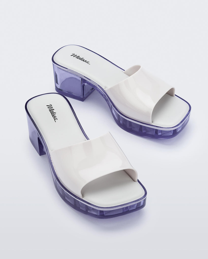 Overhead angled view of a pair of Melissa Shape slides with clear heel and white wide strap