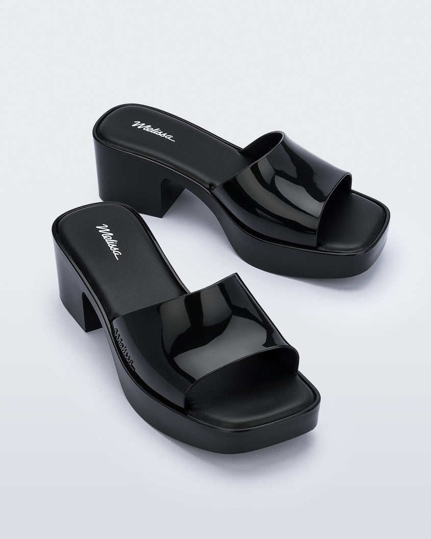 Angled view of a pair of Melissa Shape slides in black with a platform heel.