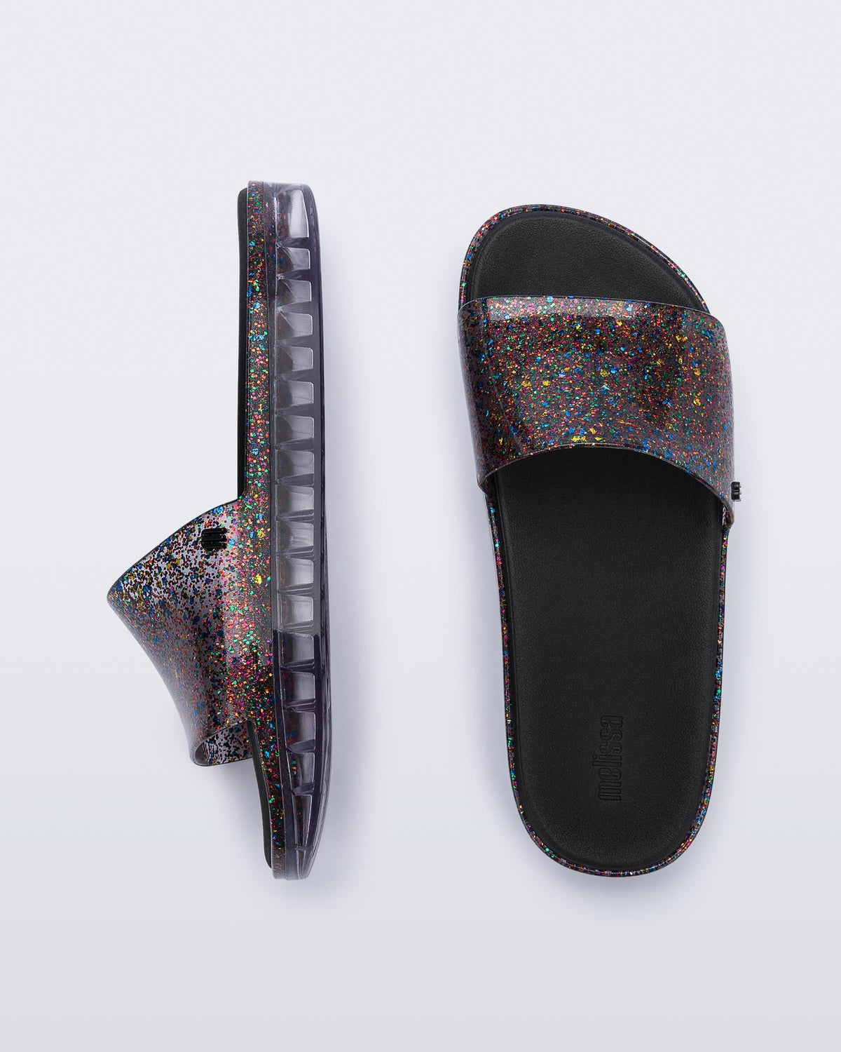 Top and side view of a pair of clear/glitter Melissa Beach slides.