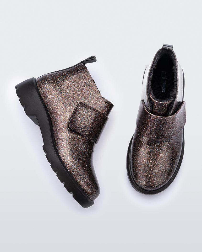 A top and side view of a pair of black/glitter multicolor Mini Melissa Chelsea boots with a glitter multicolor base, velcro front strap and black sole.