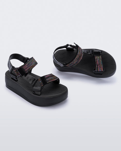 An angled side and top view of a pair of black Melissa Papete Platform sandals with a black multicolor straps.