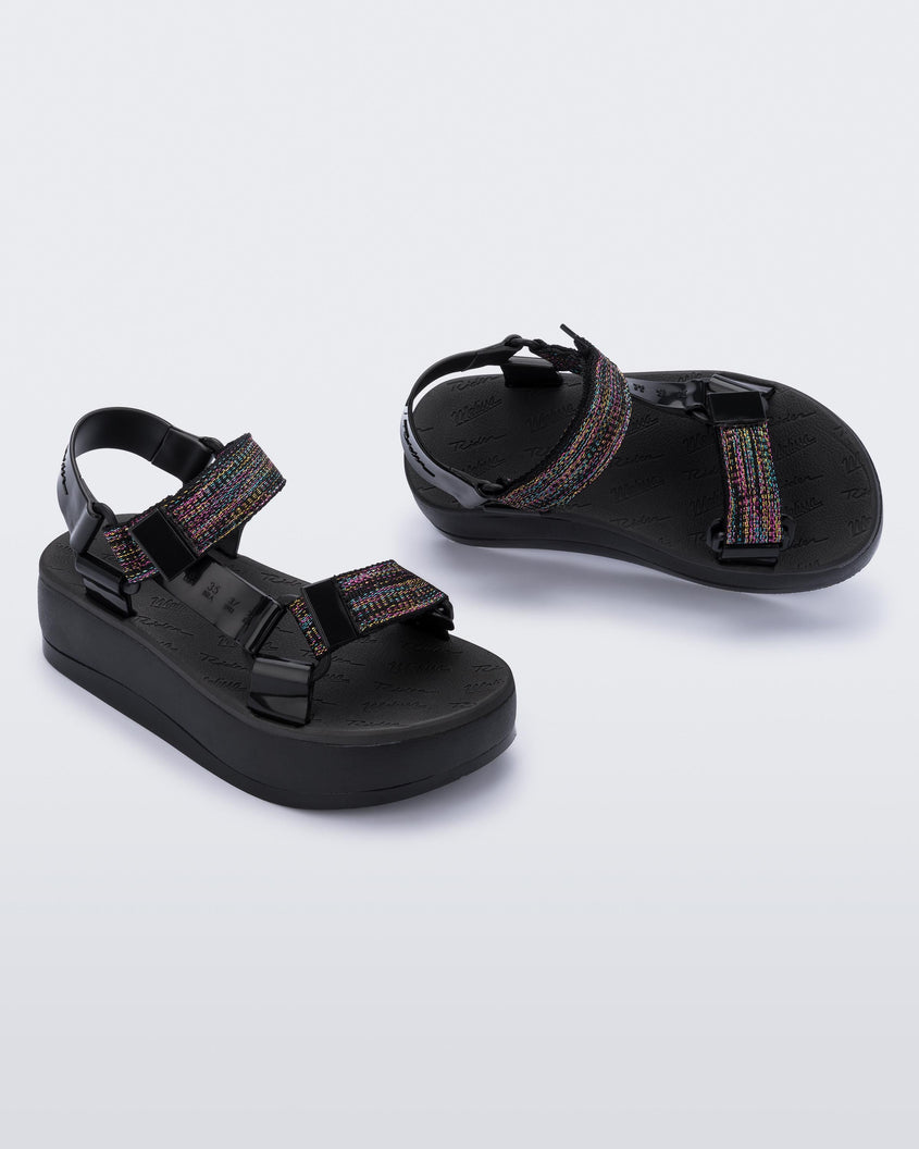 An angled side and top view of a pair of black Melissa Papete Platform sandals with a black multicolor straps.