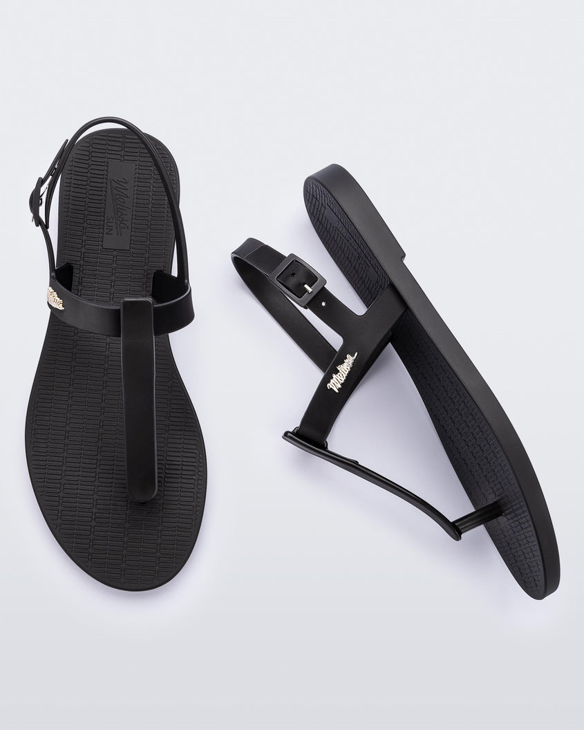 A top and side view of a pair of black Melissa Sun Ventura sandal with a top strap, reading melissa in silver, intersected by a vertical front strap detail and an ankle strap.