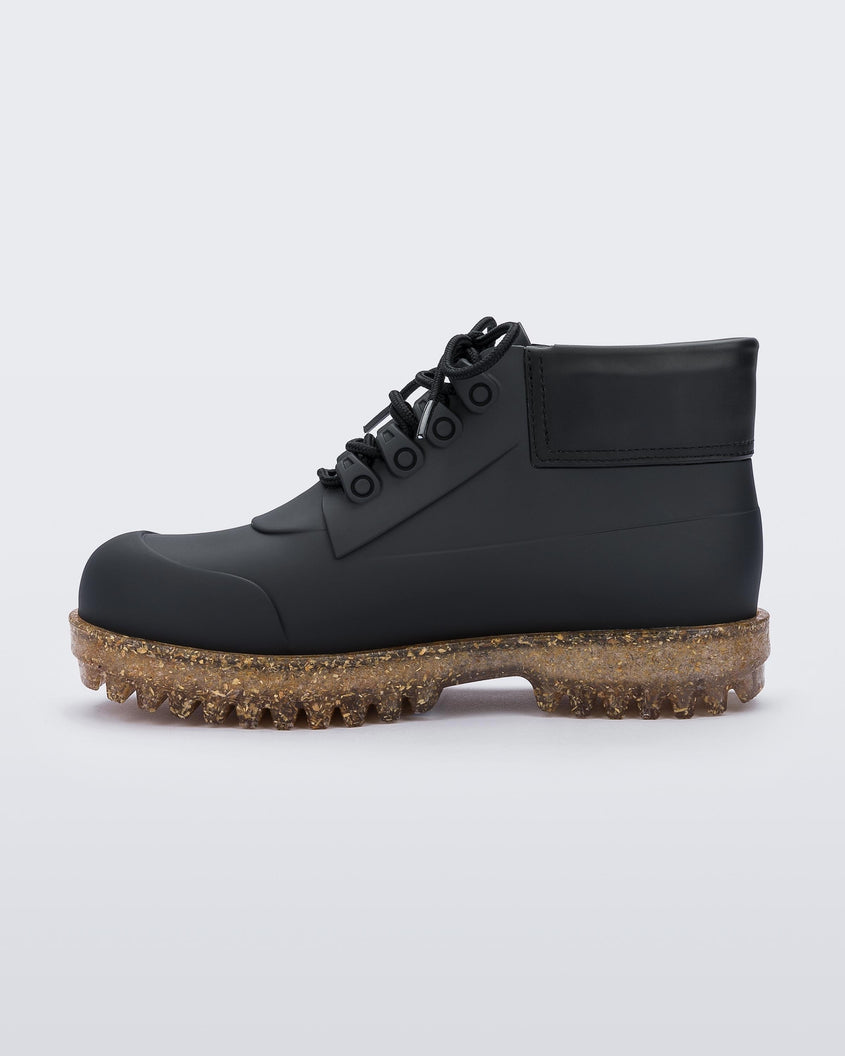 An inner side view of a matte black / rice husk Melissa Ares combat boot with a black sole, black laces and brown / gold glitter rice husk tractor sole.