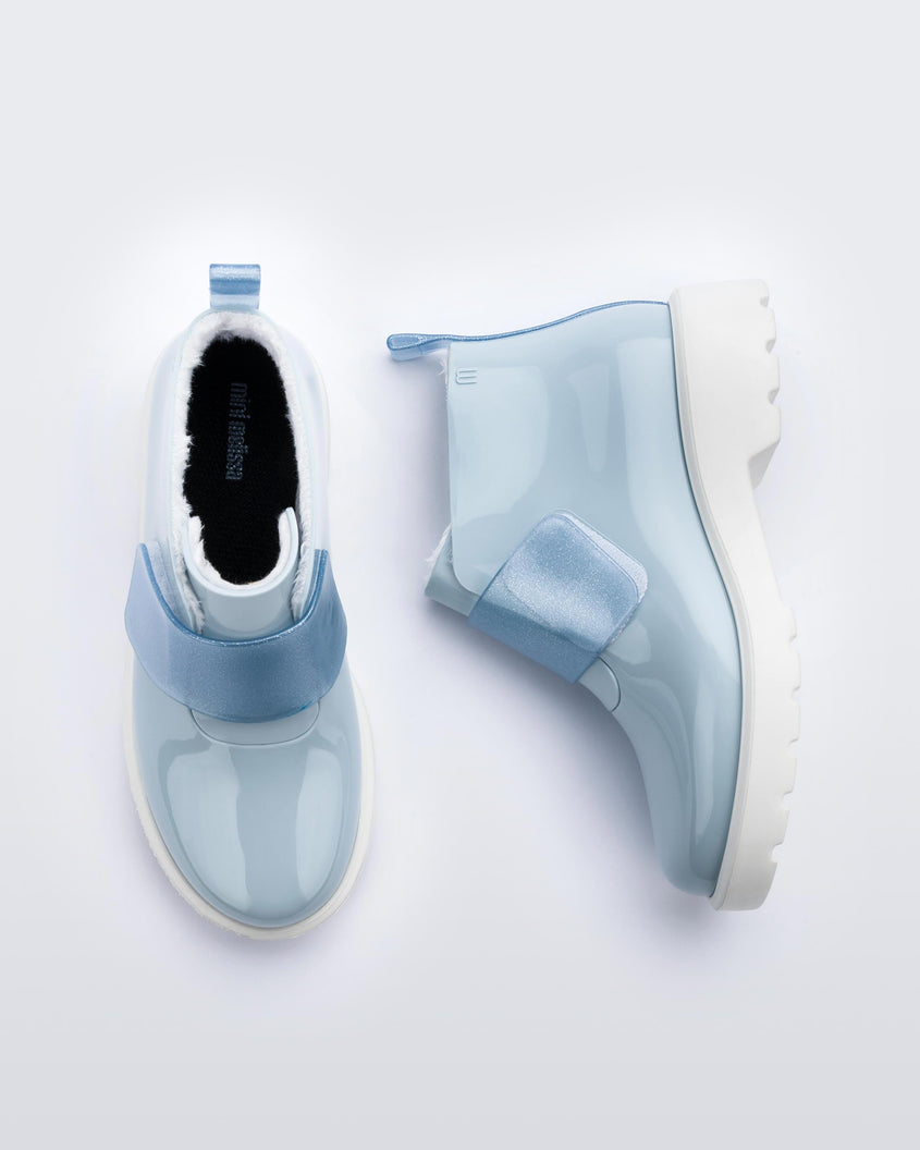 A top and side view of a pair of blue Mini Melissa Chelsea boots with a light blue base, glitter blue velcro front strap and a white sole.