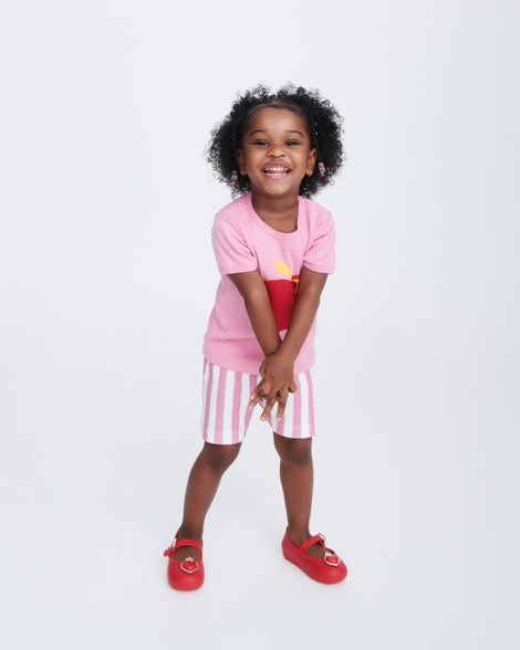 Child model in pink stripped shorts and pink shirt wearing a pair of red Soft Ballerina Princess baby flats with a red heart on top