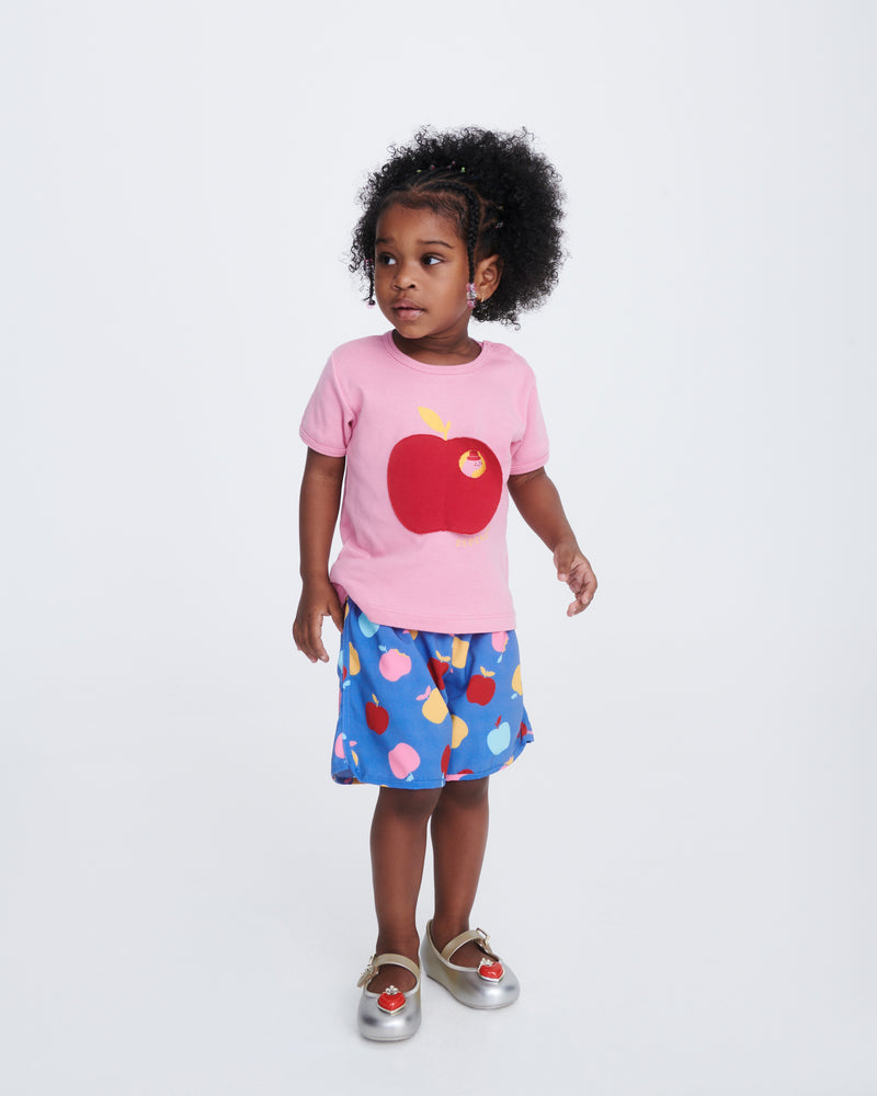 Child model in blue shorts and pink shirt wearing a pair of gold/silver Soft Ballerina Princess baby flats with a red heart on top
