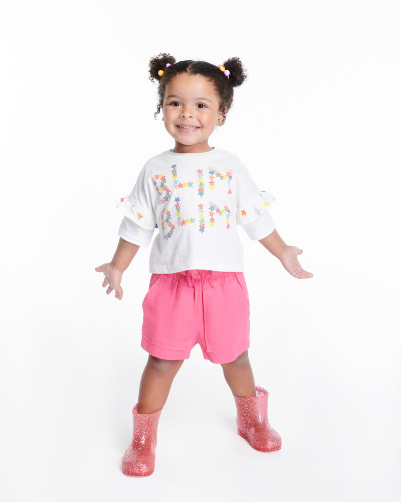 Child model in pink shorts and white shirt wearing a pair of pink glitter Welly baby rain boots