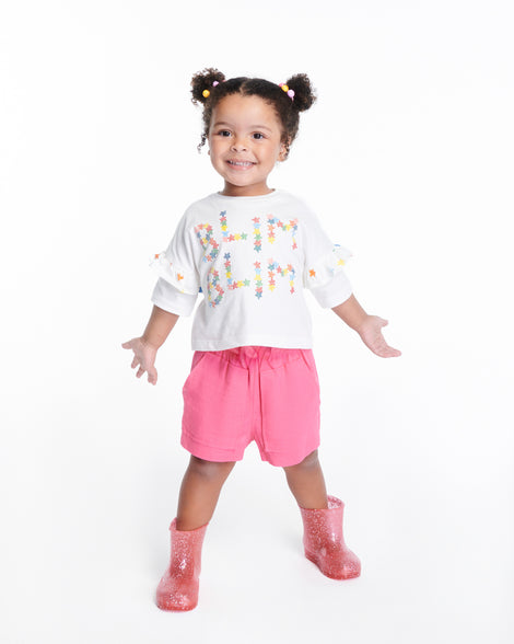 Child model in pink shorts and white shirt wearing a pair of pink glitter Welly baby rain boots